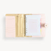 Open blush A5 vegan leather planner with, gold lining and colorful refill pages, and a gold clasp on the front cover.