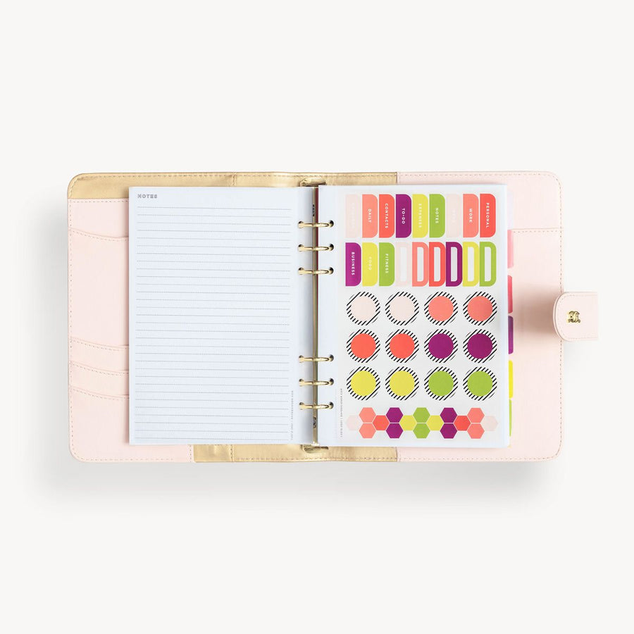 Open blush A5 vegan leather planner with, gold lining and notes pages,  colorful stickers, and a gold clasp on the front cover.
